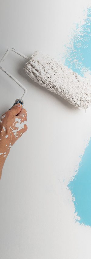 Mano de hombre con un rodillo pintado una pared azul en color blanco